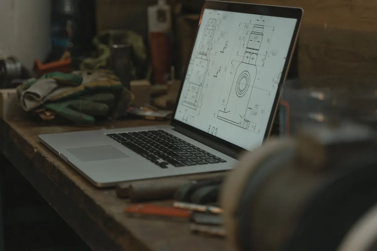 Notebook com desenho técnico cercado de ferramentas e luvas numa oficina
