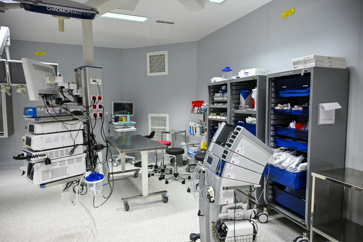 Sala cirúrgica ampla com focos cirúrgicos no teto, monitores, mesa de operação e equipamentos médicos