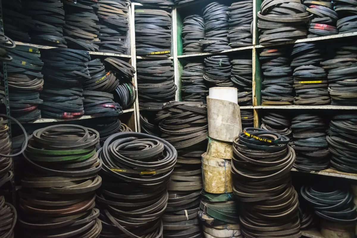 Estoque de correias em V de borracha empilhadas em prateleiras e no chão de um depósito industrial, com etiquetas de medida visíveis