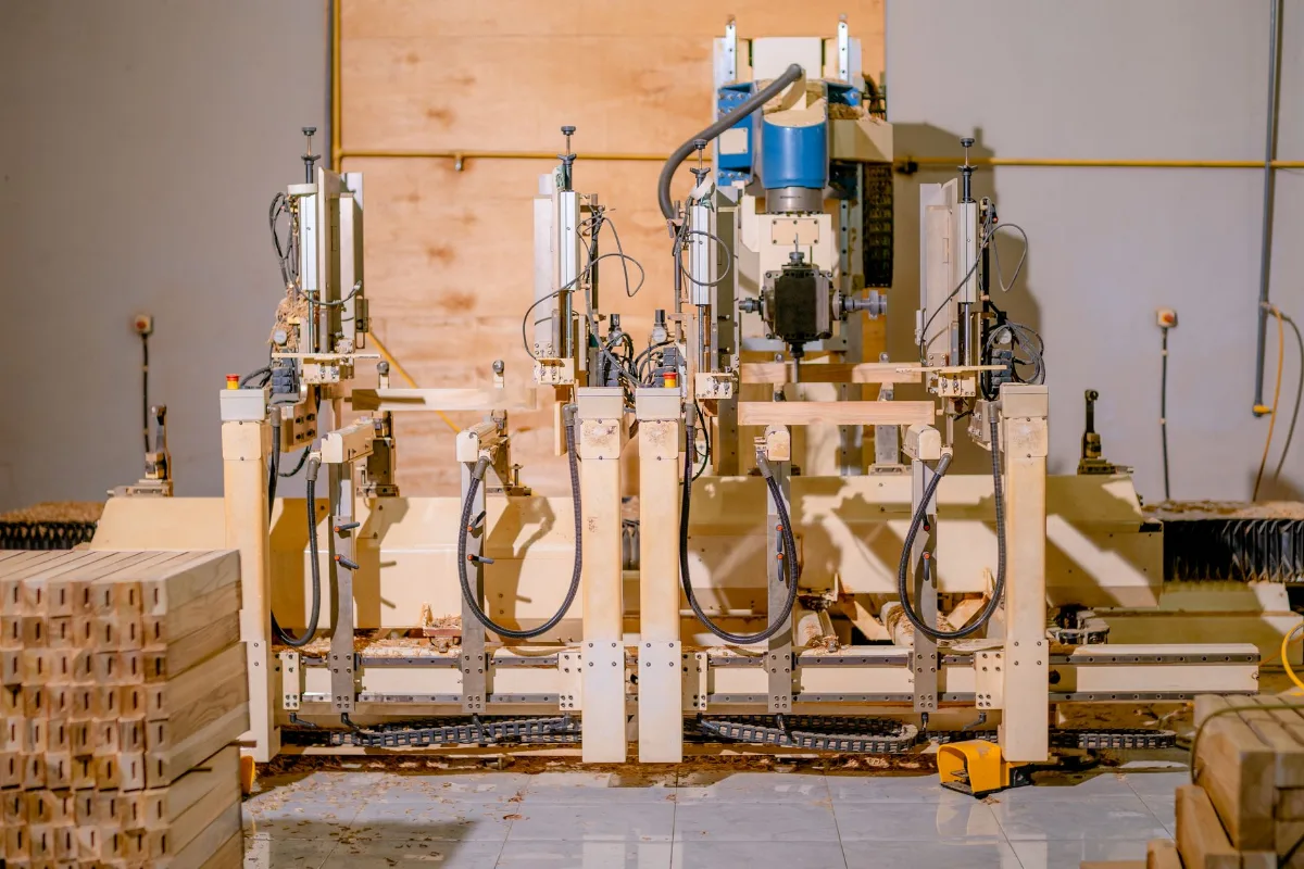 Máquina de usinagem de madeira com cabeçotes pneumáticos numa fábrica de móveis, com peças de madeira empilhadas ao lado