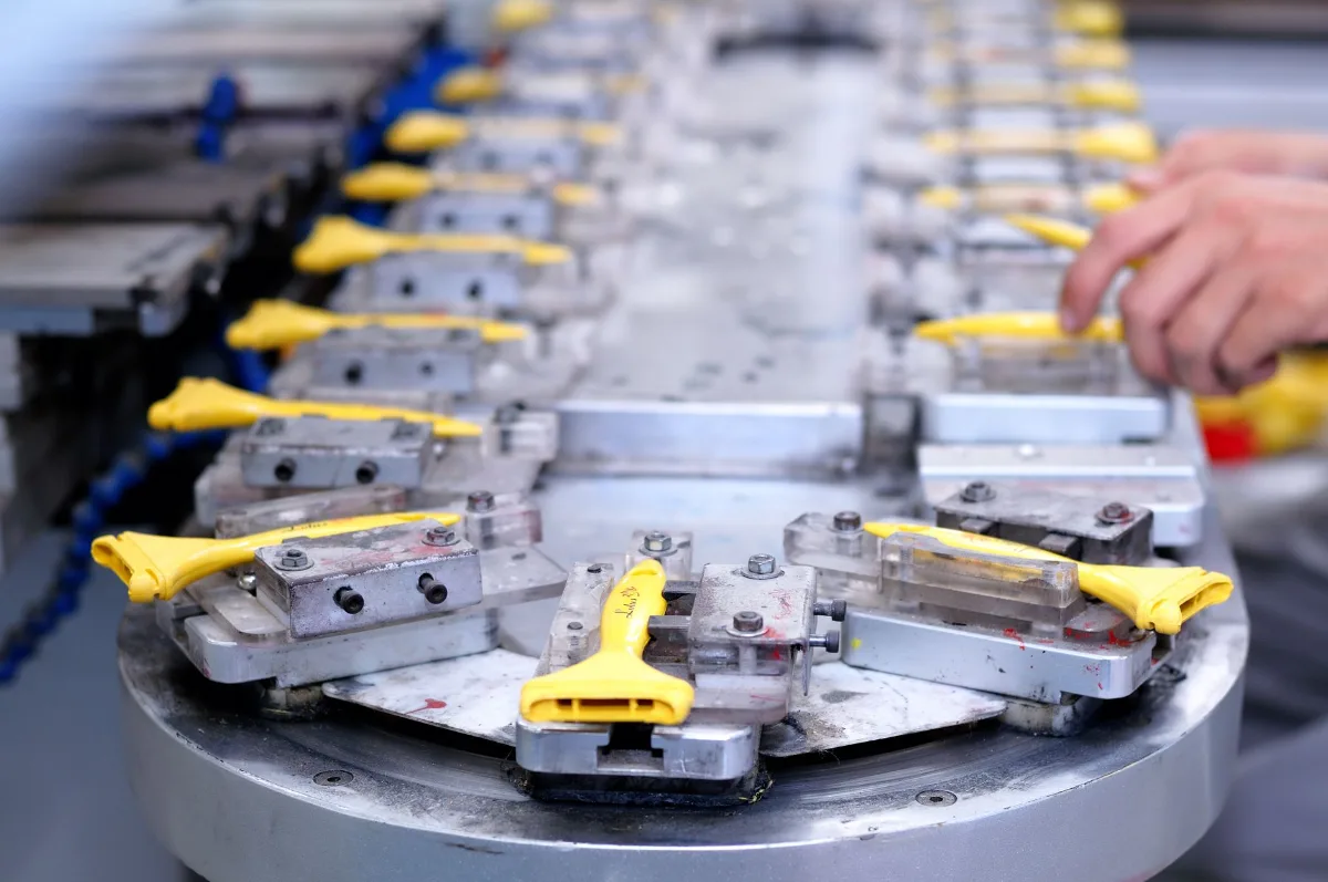 Peças plásticas amarelas presas em gabaritos metálicos numa mesa rotativa de linha de produção