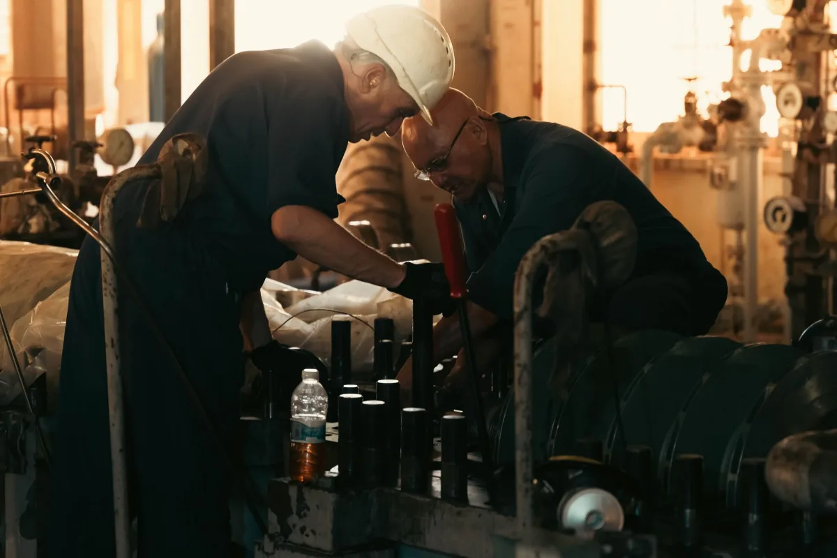 Dois técnicos de capacete fazendo manutenção em maquinário pesado numa planta industrial