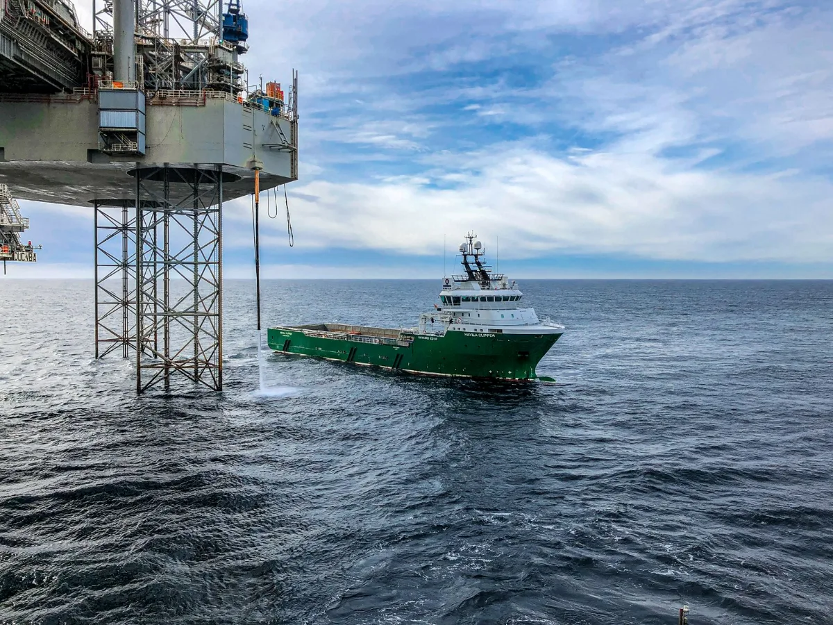 Navio de apoio offshore de casco verde se aproximando das pernas treliçadas de uma plataforma de petróleo em mar aberto