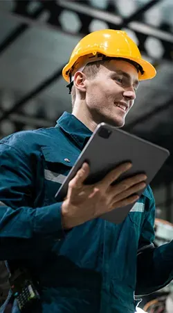 Operador de capacete sorrindo com um tablet no chão de fábrica
